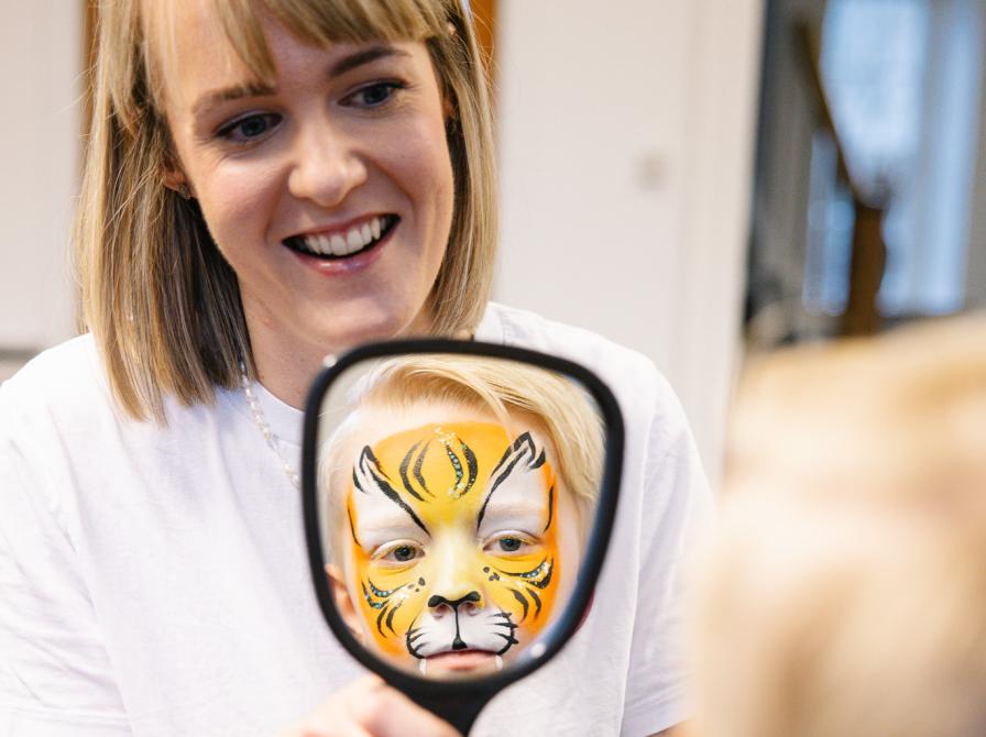 Kvinde holder spejl hvor dreng med ansigtsmalet tiger spejler sig